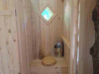 Cabane en bois dans les arbres avec une fenêtre en losange et un coin toilette.