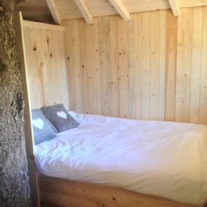 Cabane en bois dans les arbres, lit douillet avec coussins en forme de cœur.