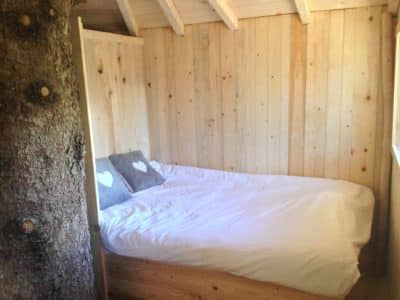 Cabane en bois dans les arbres, lit douillet avec coussins en forme de cœur.