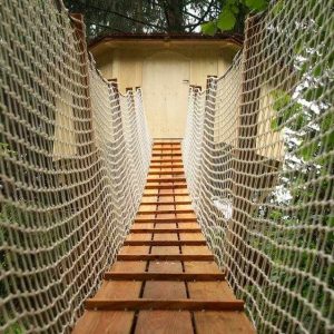 Cabane dans les arbres en Auvergne-Rhône-Alpes, accessible par un pont suspendu en bois.