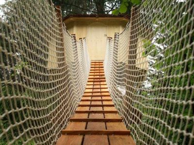 Cabane dans les arbres en Auvergne-Rhône-Alpes, accessible par un pont suspendu en bois.