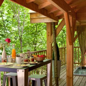 Cabane dans les arbres à Limousin, avec terrasse en bois et vue sur la nature verdoyante.