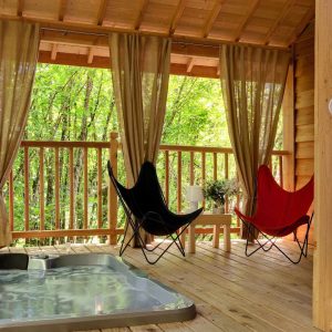 Cabane dans les arbres avec jacuzzi, fauteuils colorés et vue sur la nature verdoyante.
