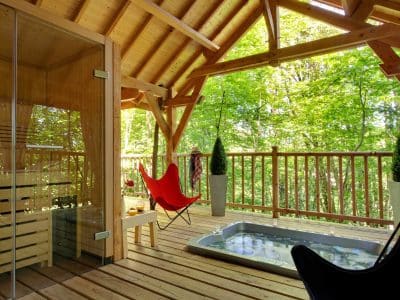 Cabane en bois avec sauna et jacuzzi, entourée de verdure apaisante.