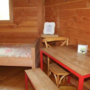 Chalet en bois chaleureux avec lit simple et table rouge accueillante.