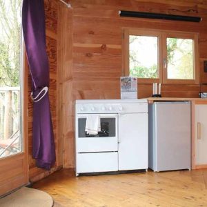 Chalet en bois avec cuisine équipée et grandes fenêtres sur la nature environnante.