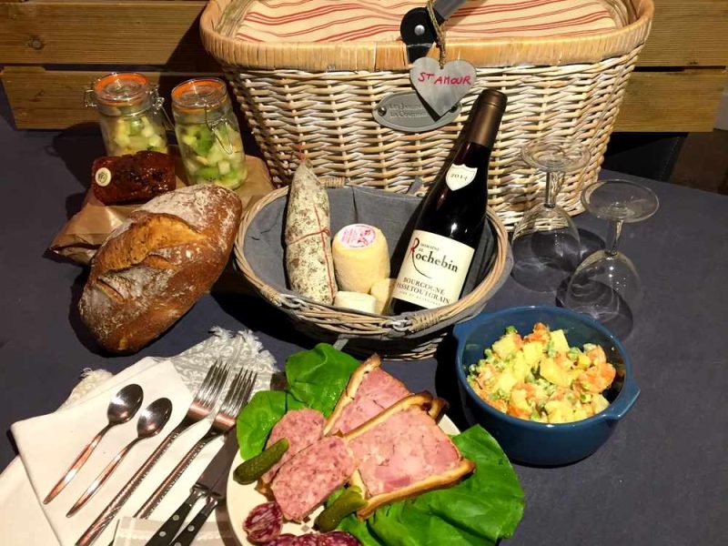 Panier pique-nique dans un hébergement, avec charcuterie, vin et salade colorée.