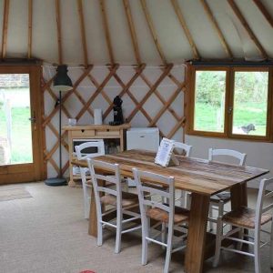 Yourte spacieuse avec un intérieur en bois, table conviviale et lumière naturelle.
