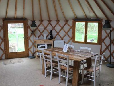Yourte spacieuse avec un intérieur en bois, table conviviale et lumière naturelle.