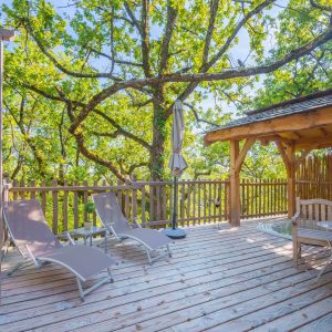 Cabane perchée en Aquitaine avec terrasse en bois et chaises longues sous les arbres.