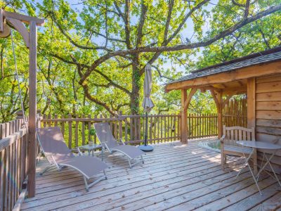 Cabane perchée en Aquitaine avec terrasse en bois et chaises longues sous les arbres.