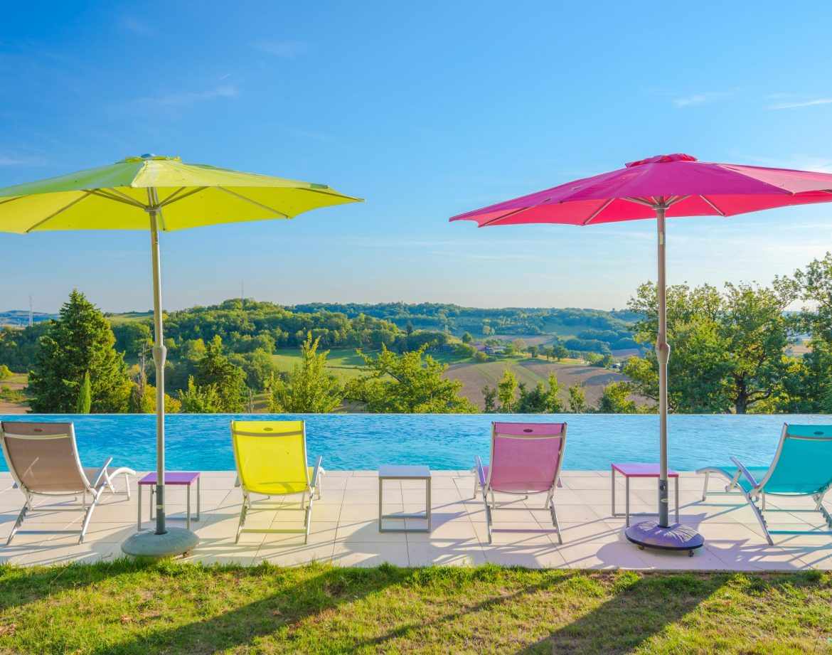 Hébergement insolite en Aquitaine avec piscine à débordement et parasols colorés.