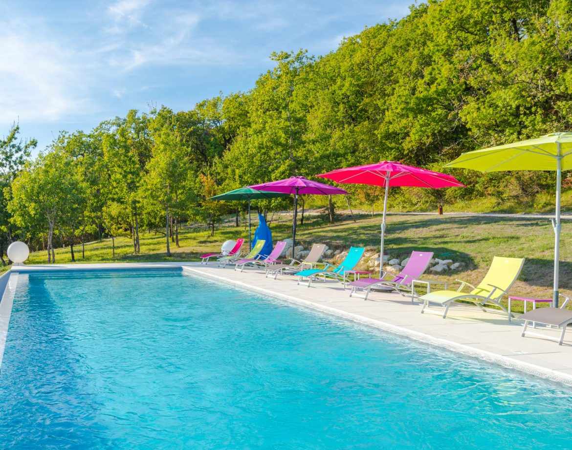 Hébergement insolite en Aquitaine avec piscine et transats colorés sous des parasols.