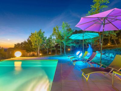 Hébergement insolite en Aquitaine avec piscine illuminée et parasols colorés.