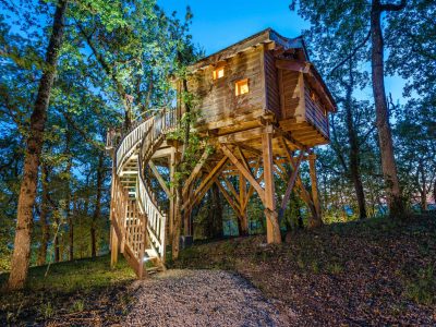 Cabane perchée en Aquitaine, illuminée, entourée darbres verdoyants.