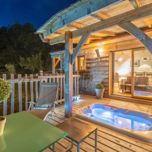 Cabane en bois avec jacuzzi sur la terrasse, ambiance nocturne apaisante.