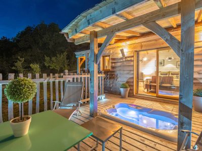 Cabane en bois avec jacuzzi sur la terrasse, ambiance nocturne apaisante.