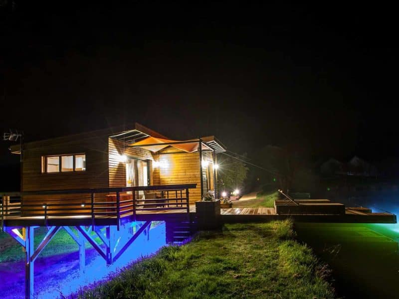 Cabane sur pilotis illuminée au bord de leau, offrant une vue nocturne paisible.
