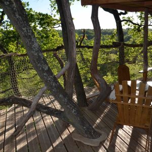 Cabane perchée dans les arbres, avec vue sur la nature et chaises en bois.