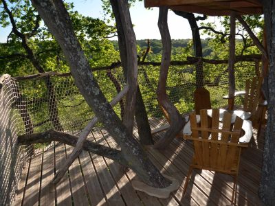 Cabane perchée dans les arbres, avec vue sur la nature et chaises en bois.