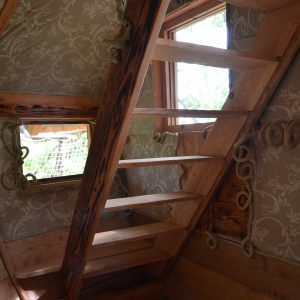 Cabane perchée en Midi-Pyrénées avec un escalier en bois et des murs décorés.
