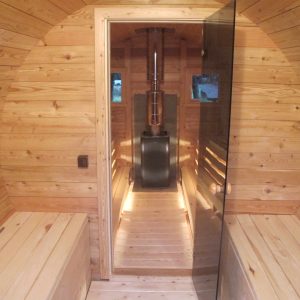 Hébergement insolite en forme de sauna en bois, avec un poêle central et un éclairage chaleureux.