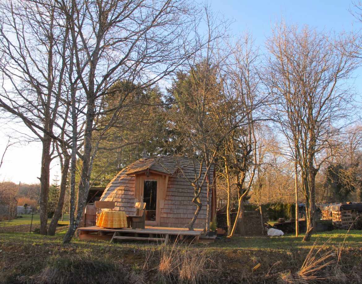 Cabane en bois à Champagne-Ardennes, entourée darbres, avec terrasse ensoleillée.