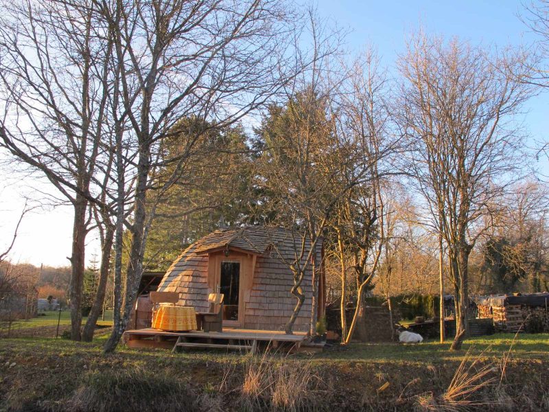 Cabane en bois à Champagne-Ardennes, entourée darbres, avec terrasse ensoleillée.
