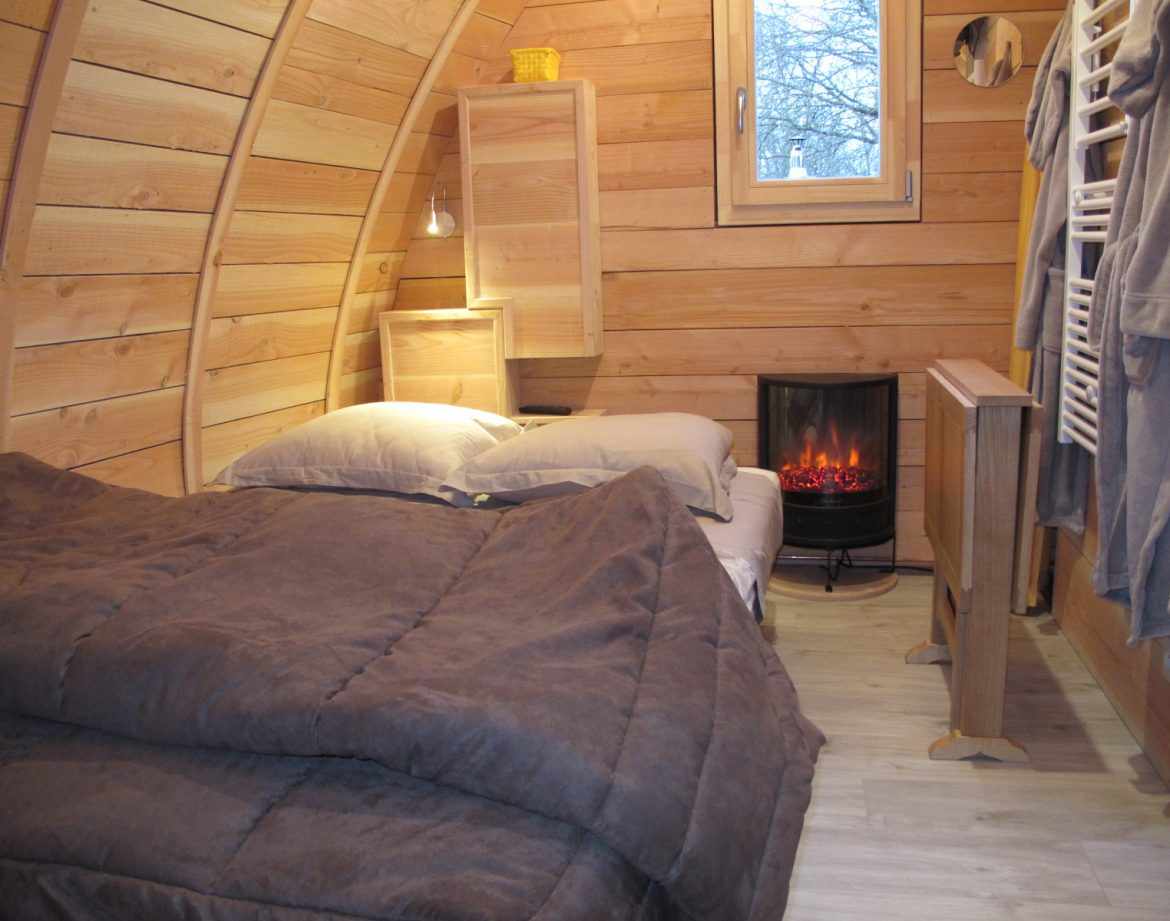 Hébergement insolite en forme de cabane en bois, avec un lit douillet et un poêle à chaleur.