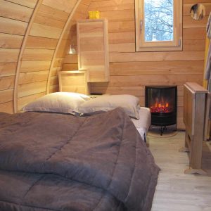 Hébergement insolite en forme de cabane en bois, avec un lit douillet et un poêle à chaleur.
