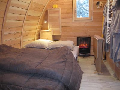 Hébergement insolite en forme de cabane en bois, avec un lit douillet et un poêle à chaleur.