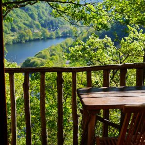 Cabane perchée dans les arbres avec vue panoramique sur la rivière et la verdure environnante.