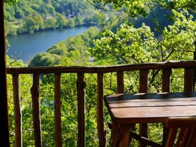 Cabane perchée dans les arbres avec vue panoramique sur la rivière et la verdure environnante.