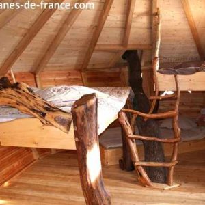 Cabane en bois dans les arbres, avec un lit en hauteur et une échelle en rondins.