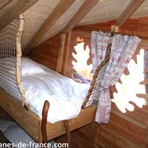 Cabane perchée en bois avec lit suspendu et fenêtres en forme de feuilles.