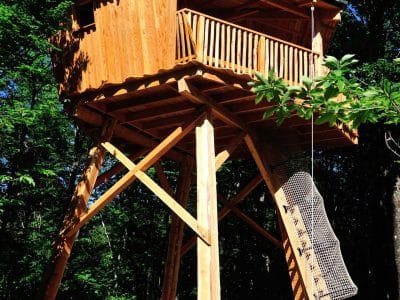 Cabane perchée en bois, entourée darbres, offrant une vue imprenable sur la nature.