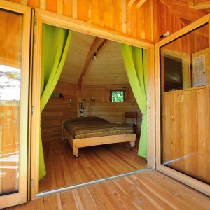 Cabane en bois avec rideaux verts, offrant une vue sur la nature environnante.