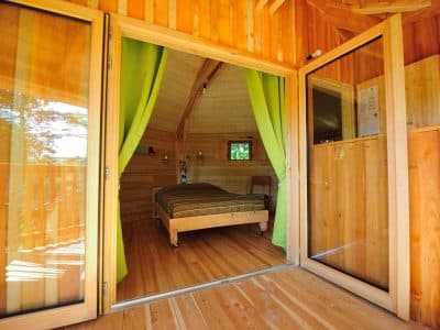 Cabane en bois avec rideaux verts, offrant une vue sur la nature environnante.