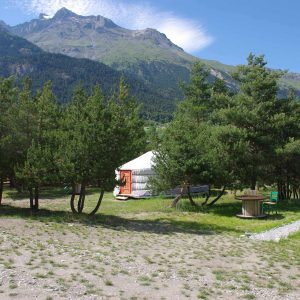 Yourtes colorées entourées de verdure, avec montagnes majestueuses en arrière-plan.