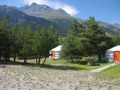 Yourtes colorées entourées de verdure, avec montagnes majestueuses en arrière-plan.