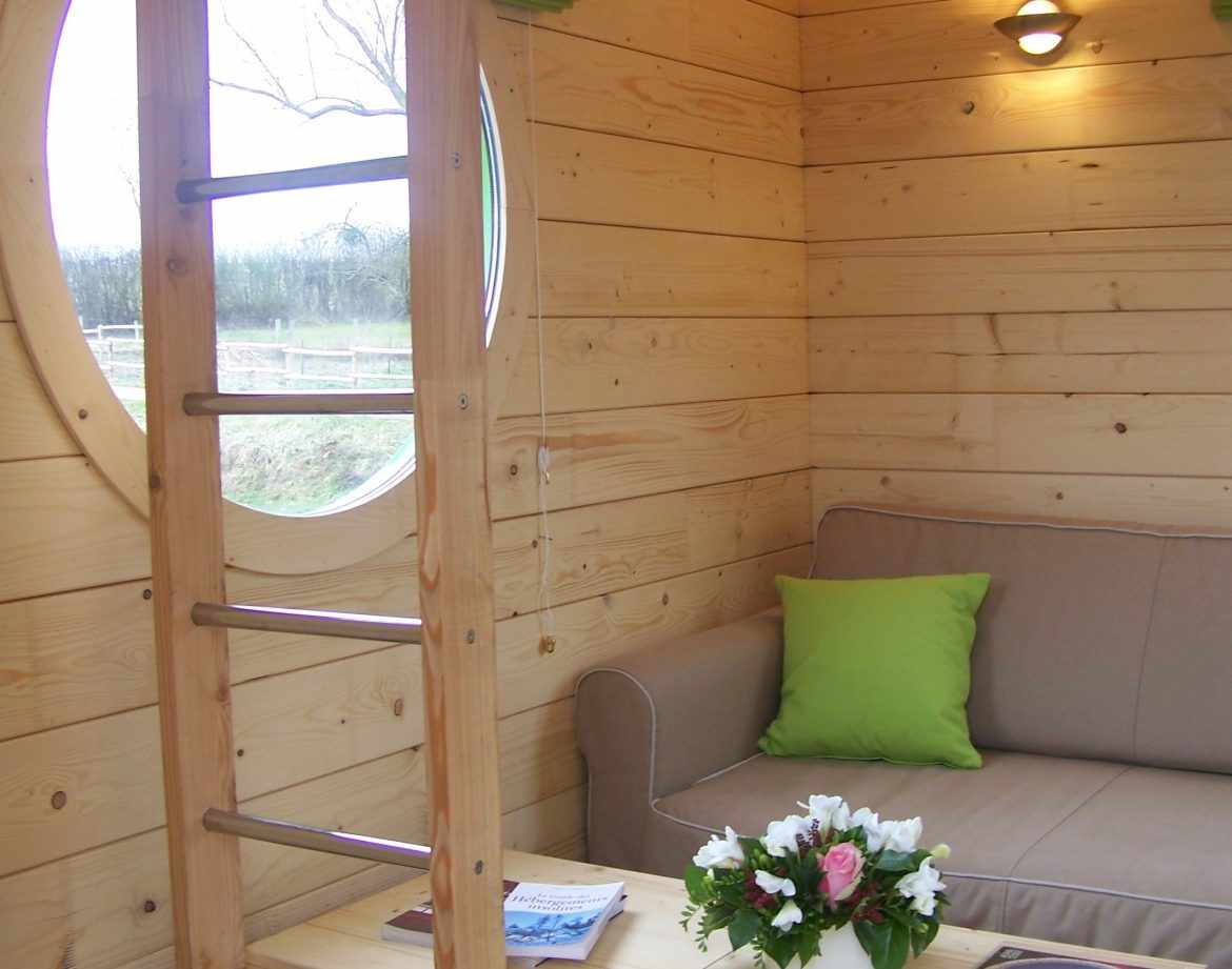Hébergement insolite en bois avec un coin salon et une fenêtre ronde.
