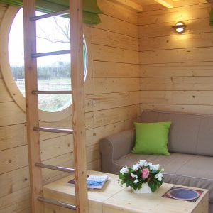 Hébergement insolite en bois avec un coin salon et une fenêtre ronde.