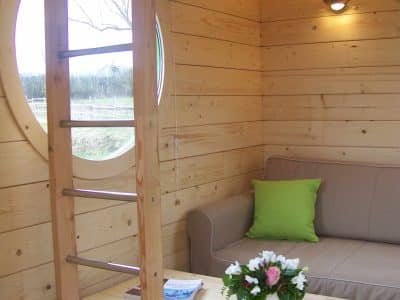 Hébergement insolite en bois avec un coin salon et une fenêtre ronde.
