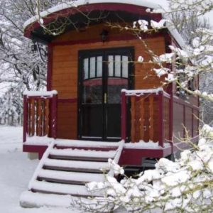 Roulotte en bois sous la neige, entourée darbres, offrant un cadre chaleureux et unique.