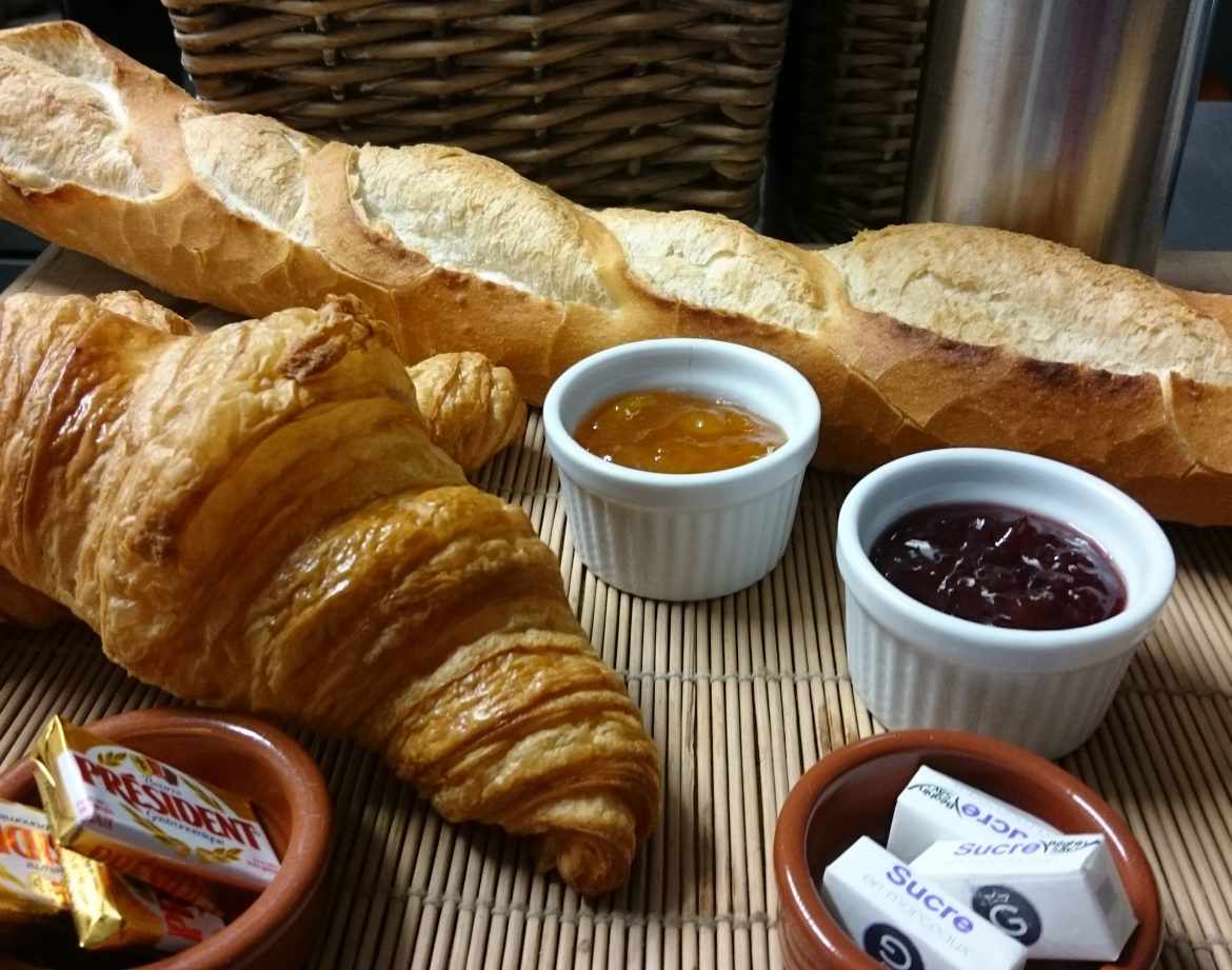 Petit-déjeuner gourmand avec croissant, baguette et confitures dans un hébergement insolite.