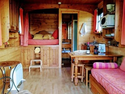 Hébergement insolite : roulotte en bois avec lit douillet et coin repas chaleureux.