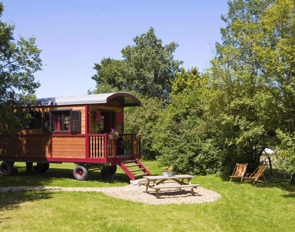 Charmante roulotte colorée entourée de verdure, avec un coin repas extérieur.