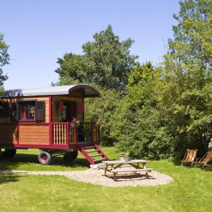 Charmante roulotte colorée entourée de verdure, avec un coin repas extérieur.