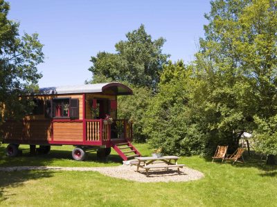 Charmante roulotte colorée entourée de verdure, avec un coin repas extérieur.