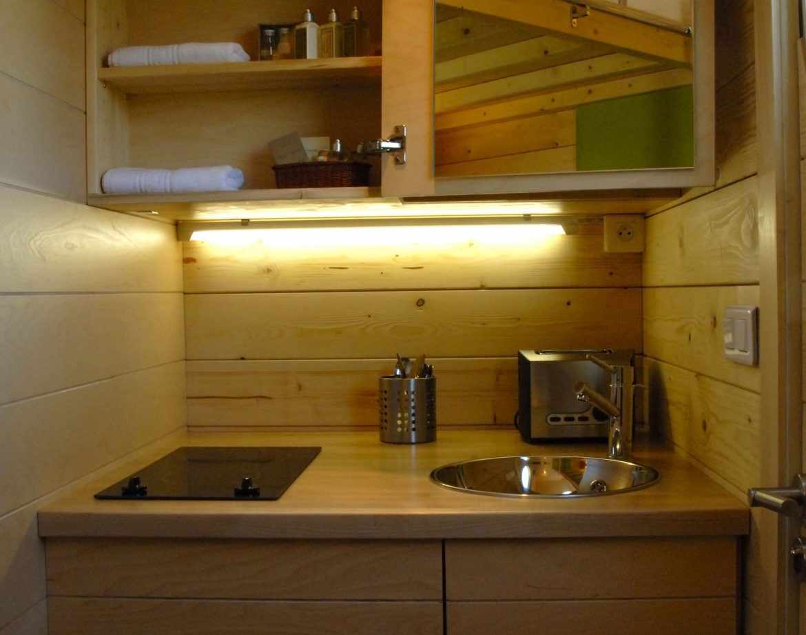 Hébergement insolite en bois avec kitchenette moderne et éclairage chaleureux.